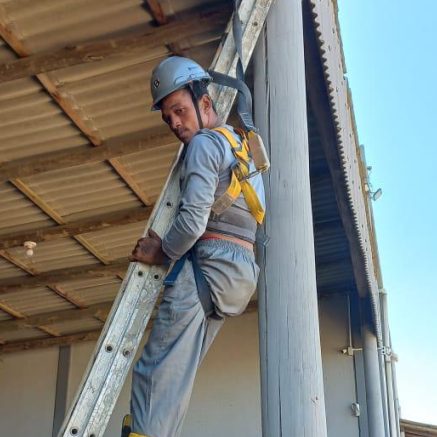 Trabalhador com cinto de segurança em escada fixa durante treinamento de NR-35