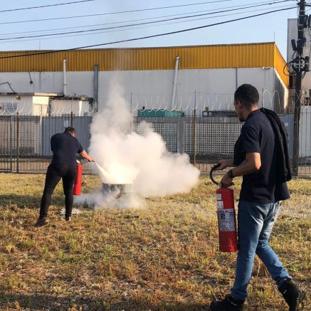 Instrutor orientando uso de extintor com fumaça ao fundo